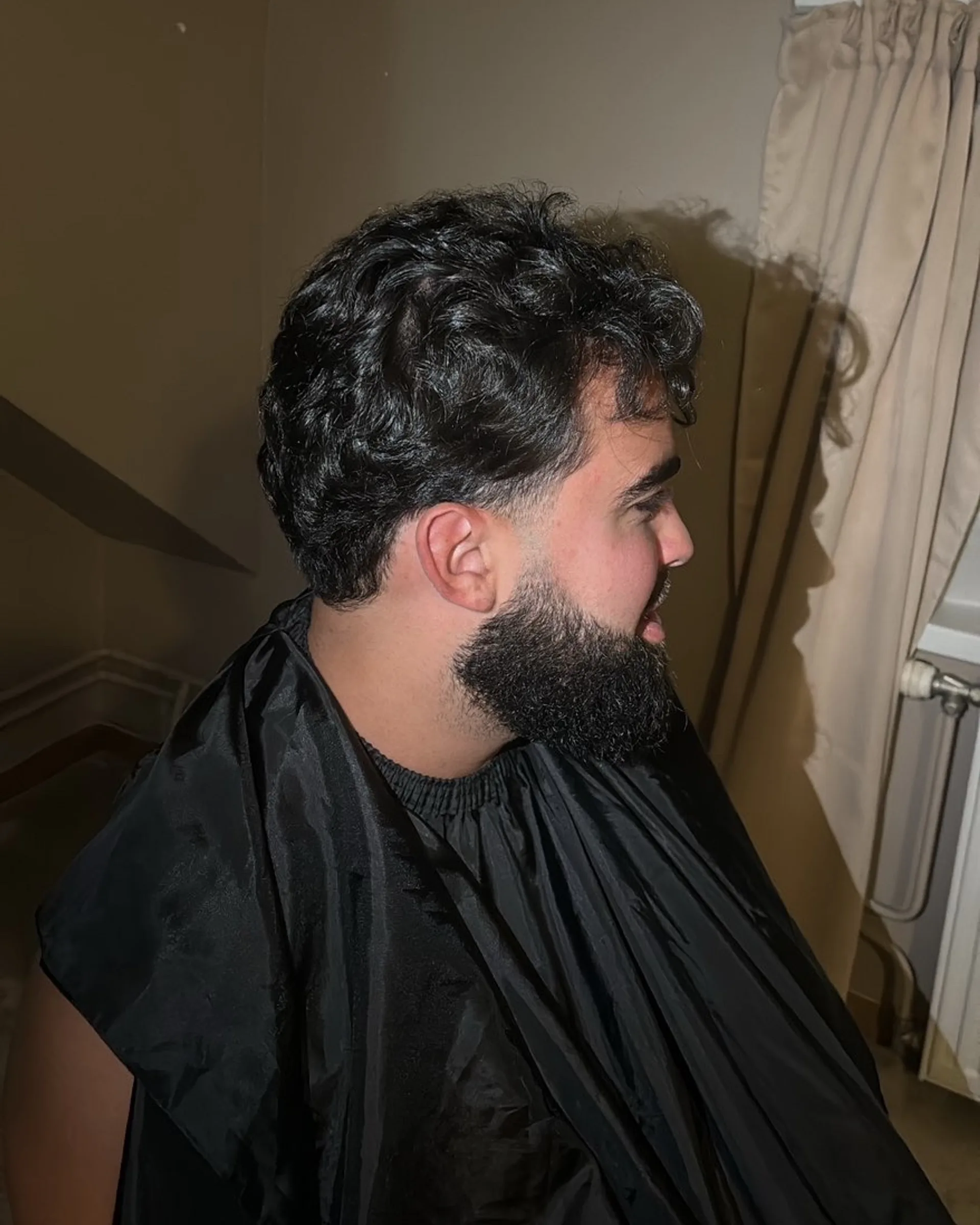 Cheveux ondulés sur le dessus avec des côtés courts, rejoignant une barbe nettement dessinée.