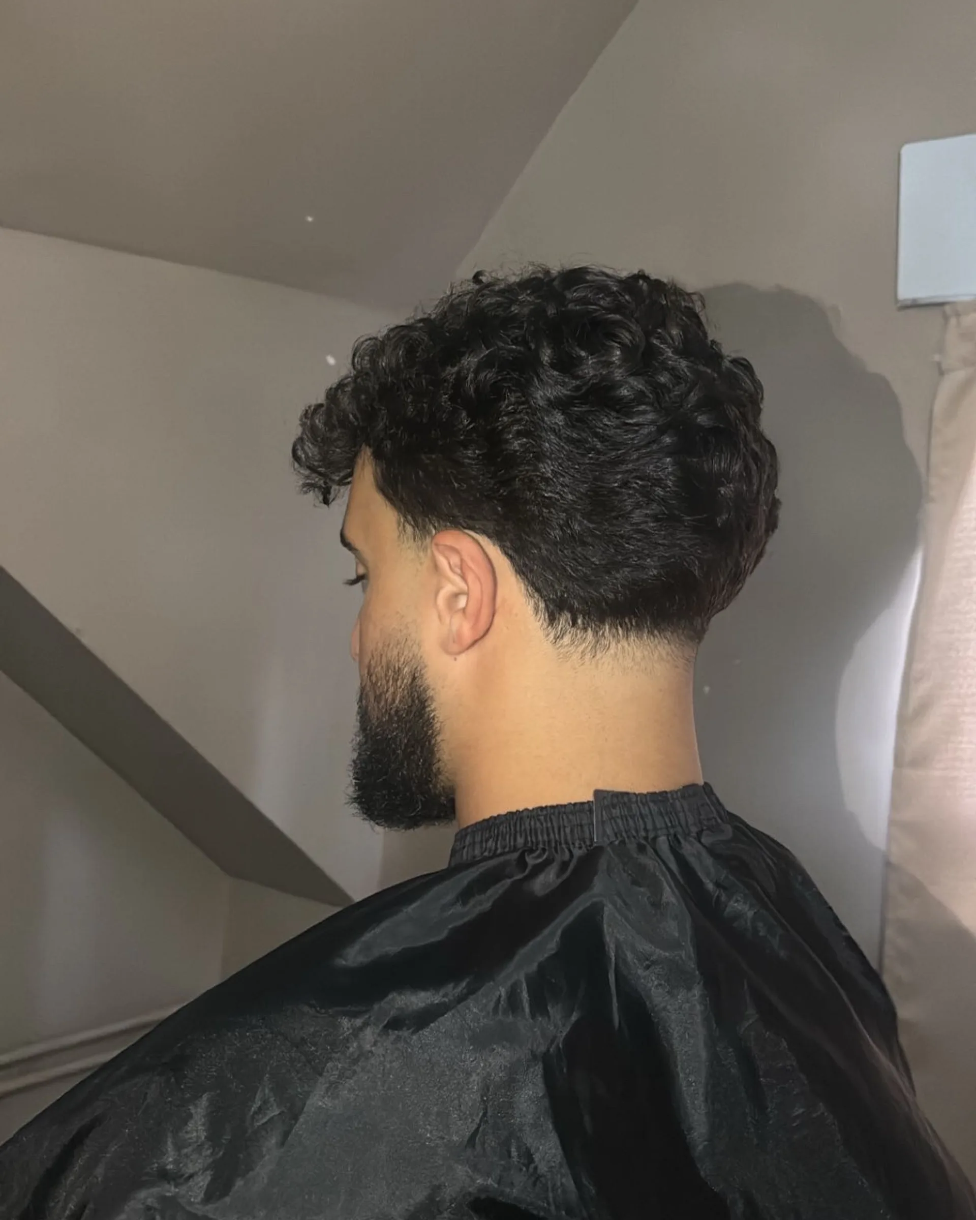 Rear view of curly hair with a cleanly finished neckline running into a trimmed beard.